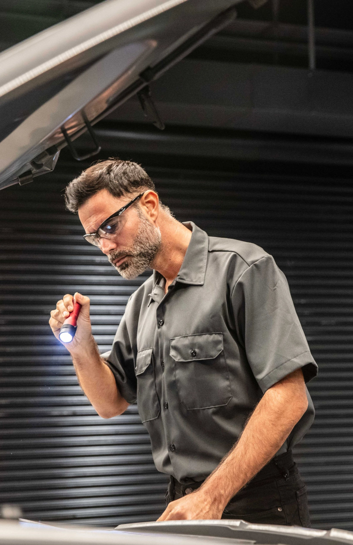 Service technician inspecting an engine with a flashlight in a service bay.
