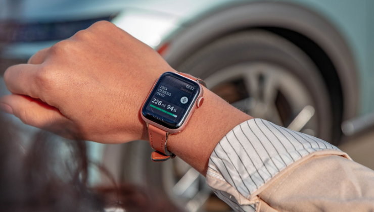 Smartwatch displaying Genesis Intelligent Assistant app near vehicle wheel.