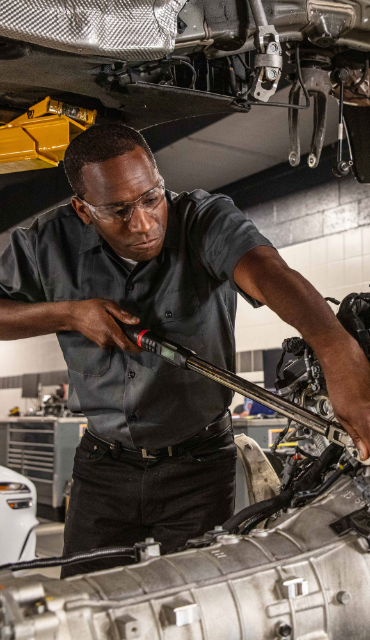 Genesis technician servicing vehicle engine inside service center.