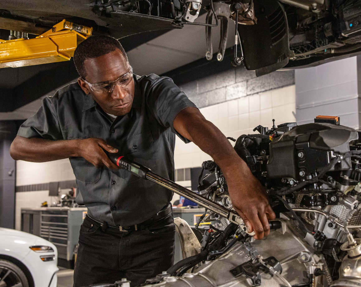Genesis technician servicing vehicle engine inside service center.