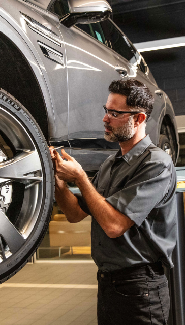 Genesis technician inspecting wheel and tire inside service center.