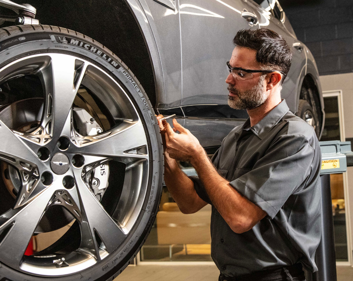 Genesis technician inspecting wheel and tire inside service center.