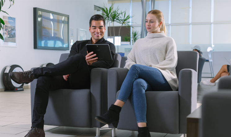 Hyundai service advisor shows tablet to customer in lounge area.