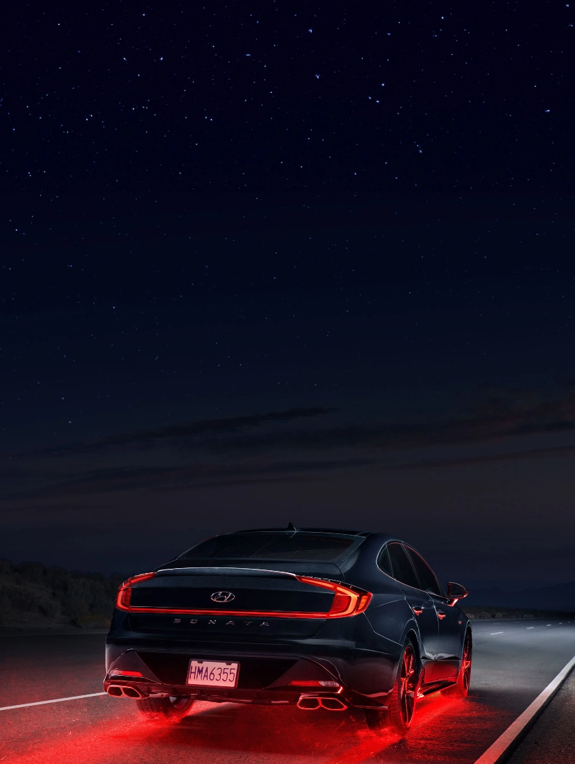 Rear view of a Hyundai Sonata driving at night with illuminated red brake lights on a desert road.