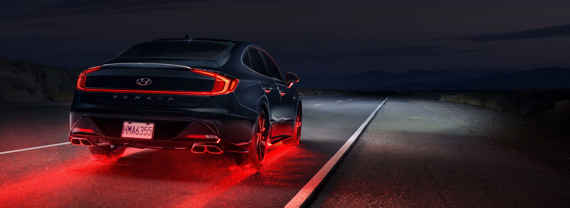 Rear view of a Hyundai Sonata driving at night with illuminated red brake lights on a desert road.