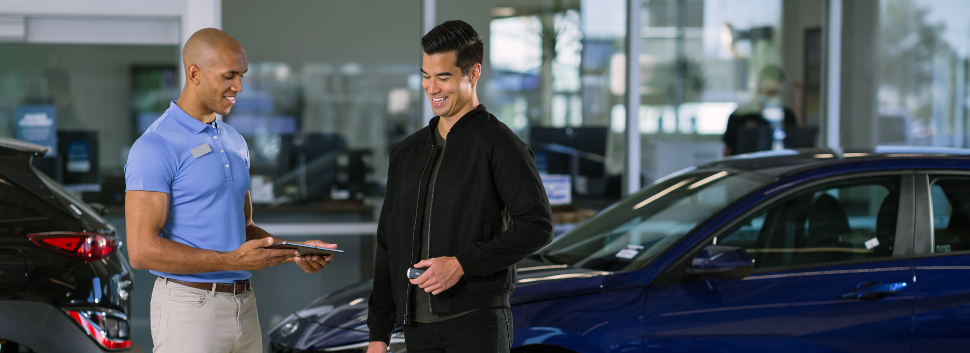Hyundai salesperson handing over car keys to a customer in a dealership showroom.