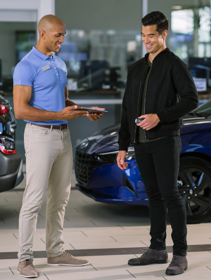 Hyundai salesperson handing over car keys to a customer in a dealership showroom.
