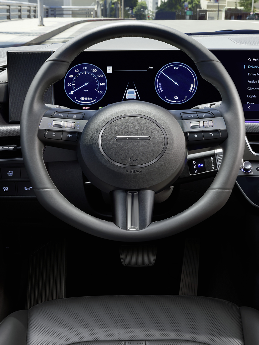Interior view of a Hyundai vehicle’s digital dashboard and steering wheel, displaying driver assistance and vehicle settings on-screen.