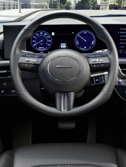 Interior view of a Hyundai vehicle’s digital dashboard and steering wheel, displaying driver assistance and vehicle settings on-screen.