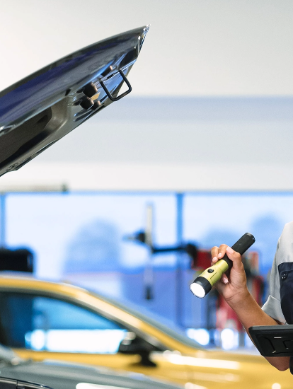 Hyundai technician inspecting a vehicle with a flashlight and tablet in a service center.