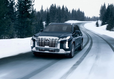 Hyundai SUV driving on a snowy road surrounded by pine trees.