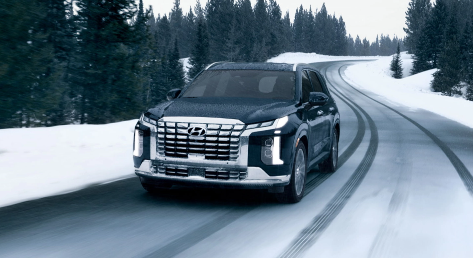 Hyundai SUV driving on a snowy road surrounded by pine trees.