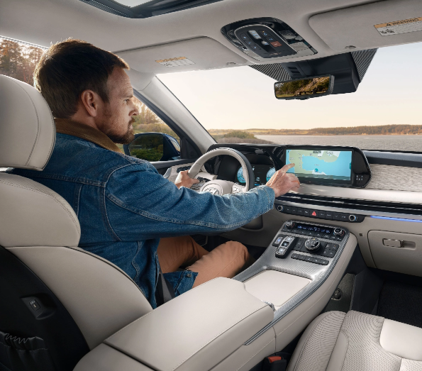 Person interacting with the touchscreen in the interior of a Hyundai vehicle, with a scenic background visible through the window.