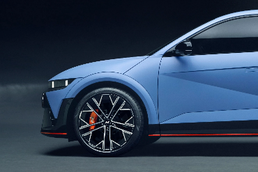 Side view of a blue Hyundai N model with sleek black alloy wheels and a sporty design, set against a dark background.