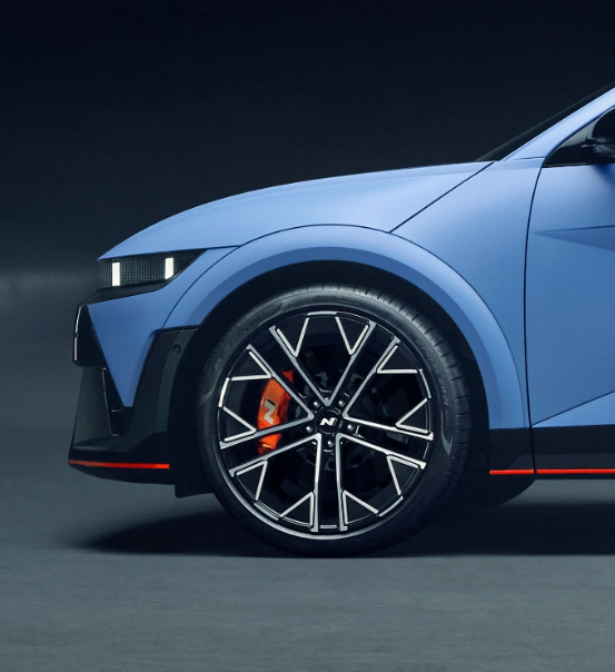 Side view of a blue Hyundai N model with sleek black alloy wheels and a sporty design, set against a dark background.