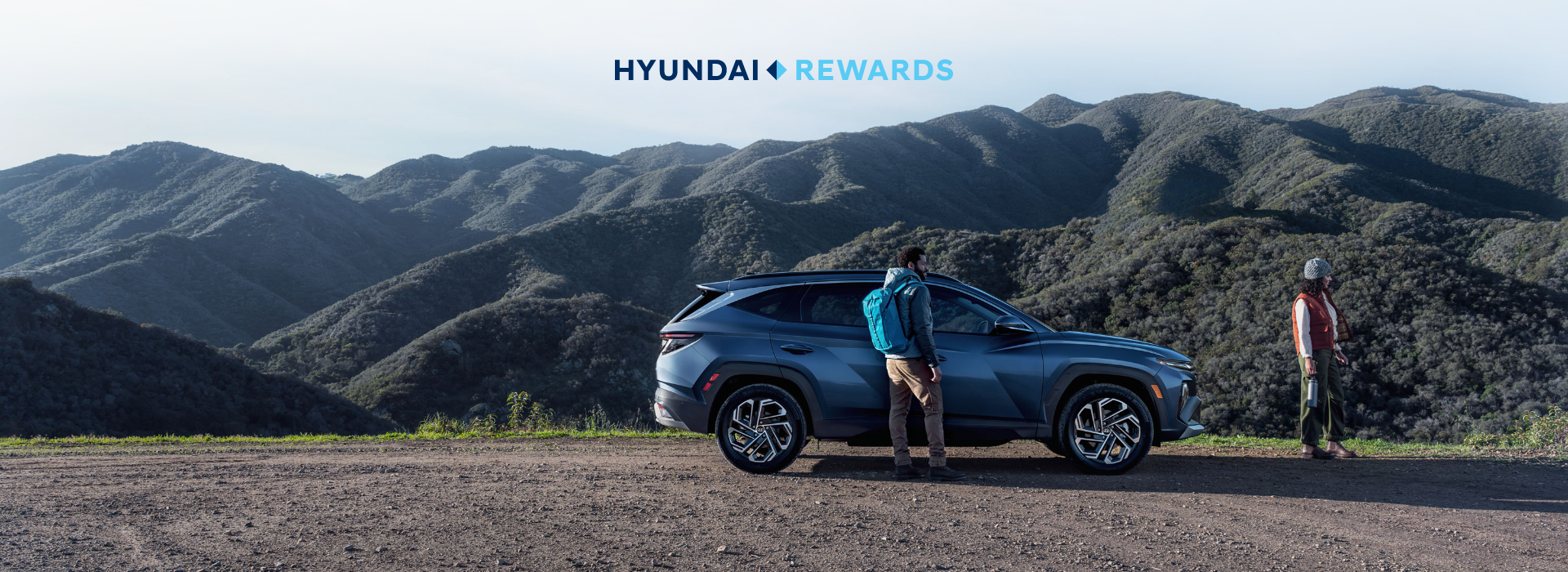 Two people stand near a Hyundai SUV overlooking a mountain landscape, representing Hyundai Rewards