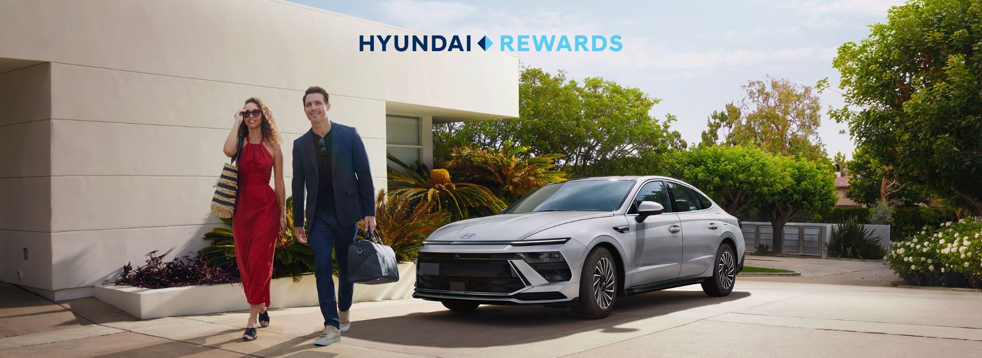Hyundai Rewards – smiling couple walking from a modern home toward a silver Hyundai sedan parked in the driveway.