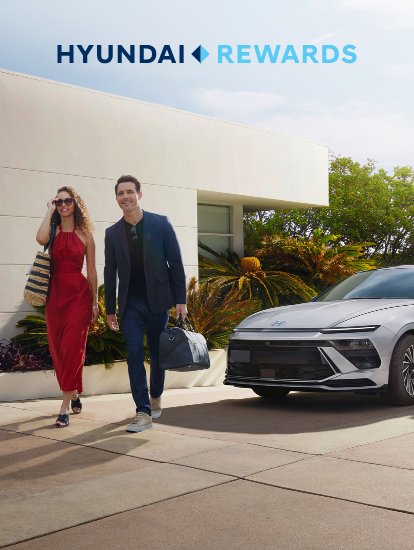 Hyundai Rewards – smiling couple walking from a modern home toward a silver Hyundai sedan parked in the driveway.