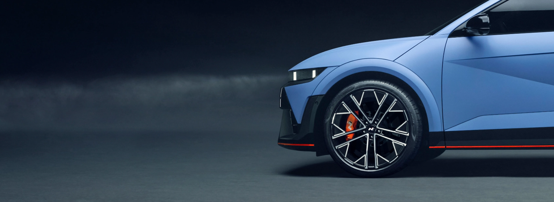 Side view of a blue Hyundai N model with sleek black alloy wheels and a sporty design, set against a dark background.