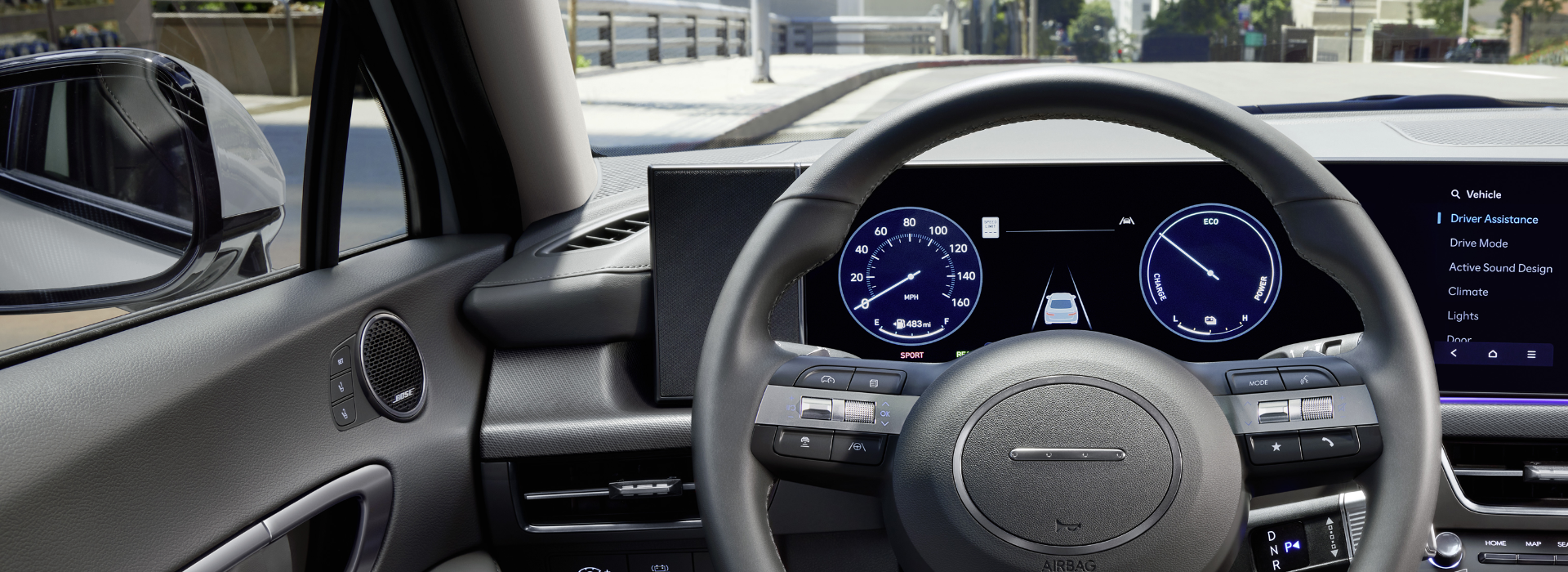 Interior view of a Hyundai vehicle’s digital dashboard and steering wheel, displaying driver assistance and vehicle settings on-screen.