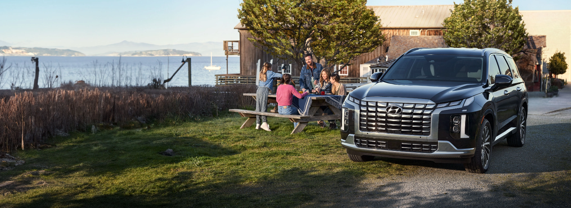 Family enjoying a picnic next to a black Hyundai SUV parked by the water.