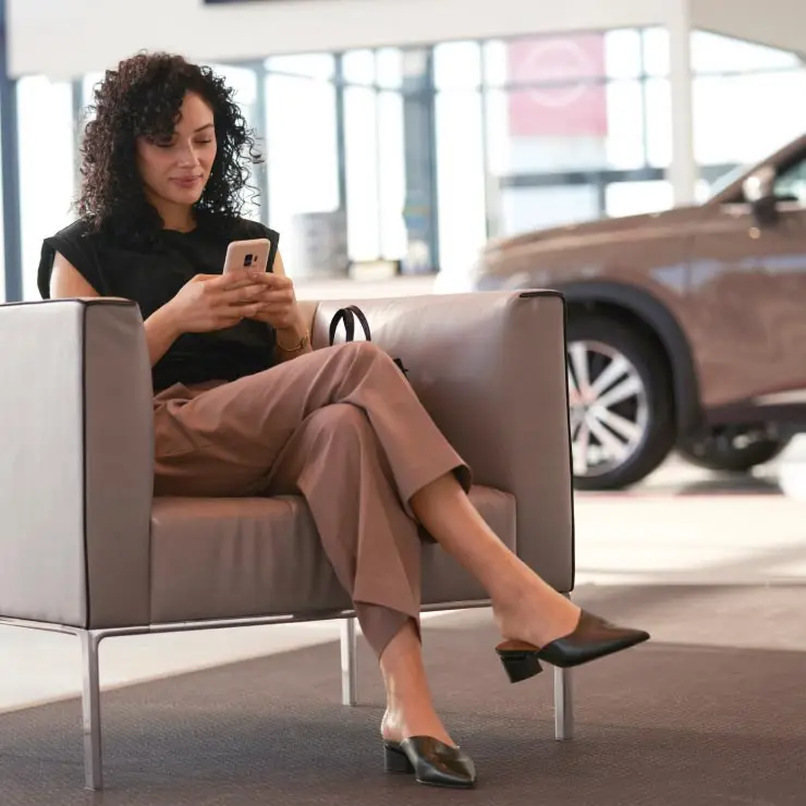 Satisfied Nissan customer inside dealership sharing her positive experience online using her mobile phone