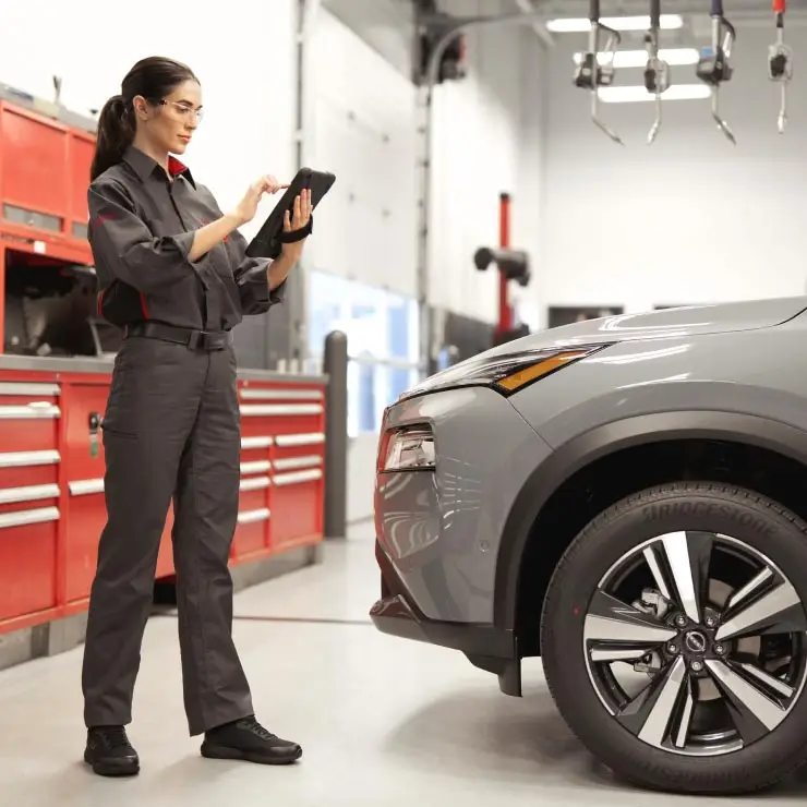 Nissan-trained technician conducting a multi-point inspection on a car inside garage