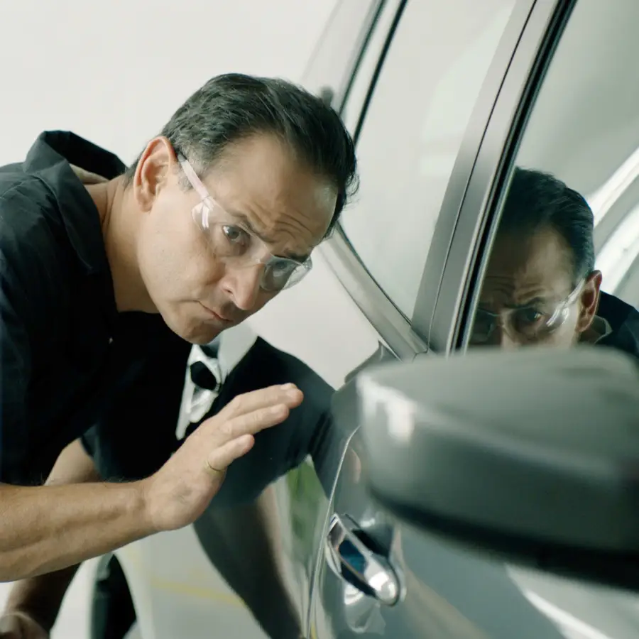 Technician closely inspecting the side of a car while wearing safety glasses.