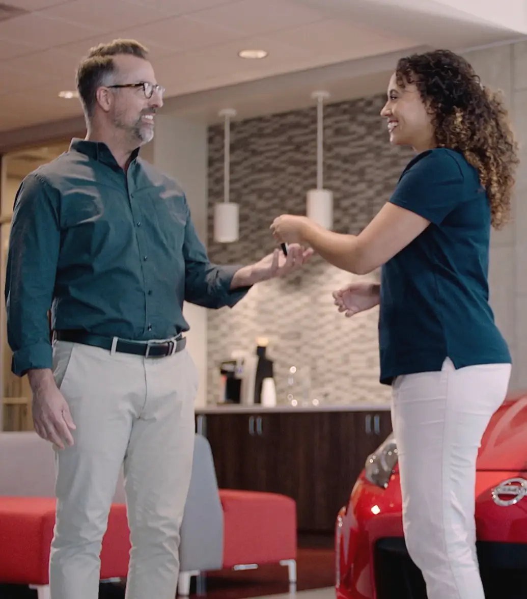 Smiling woman handing car keys to a man in a dealership.