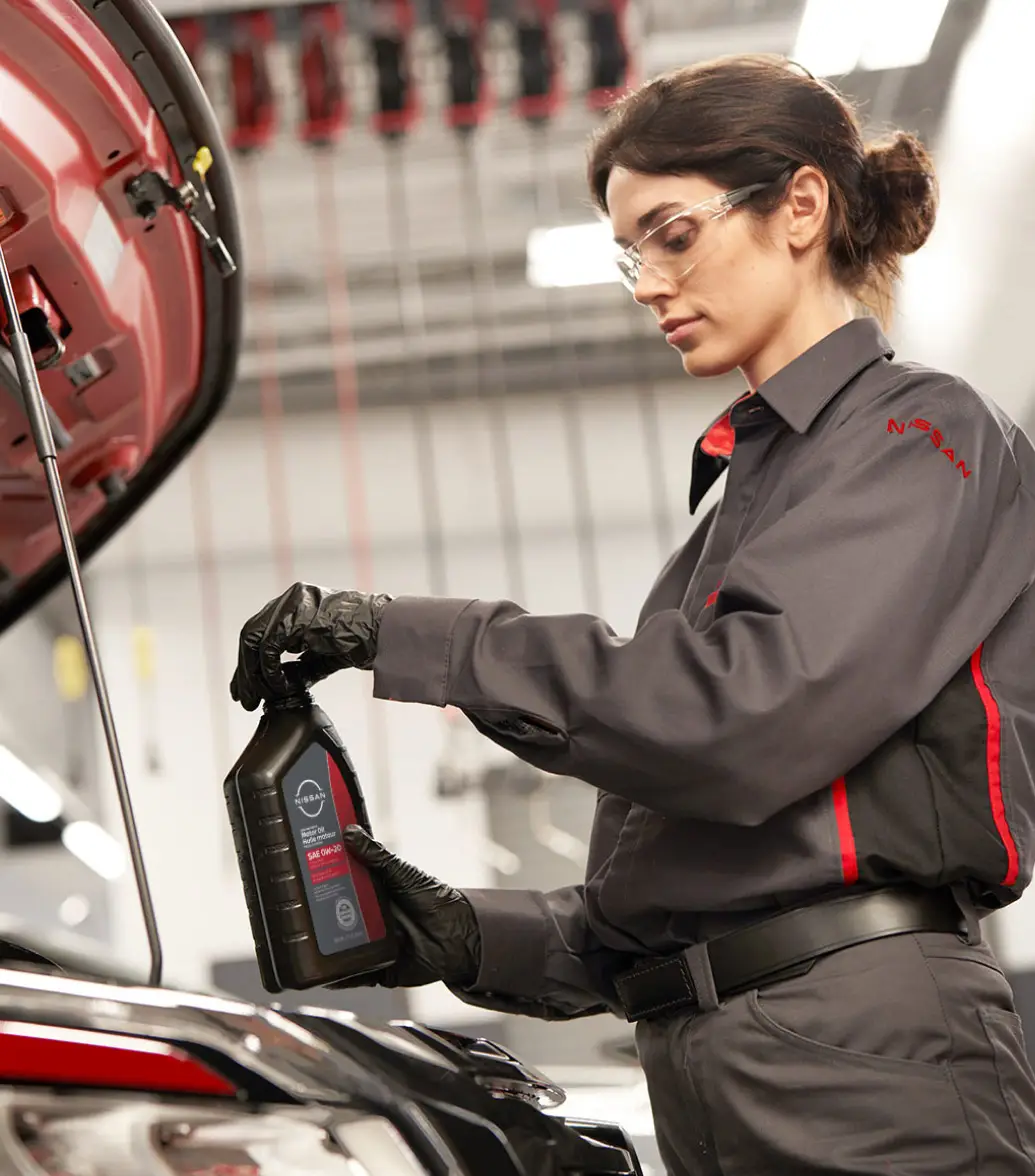 Nissan-trained technician preparing to pour engine oil into vehicle with hood raised