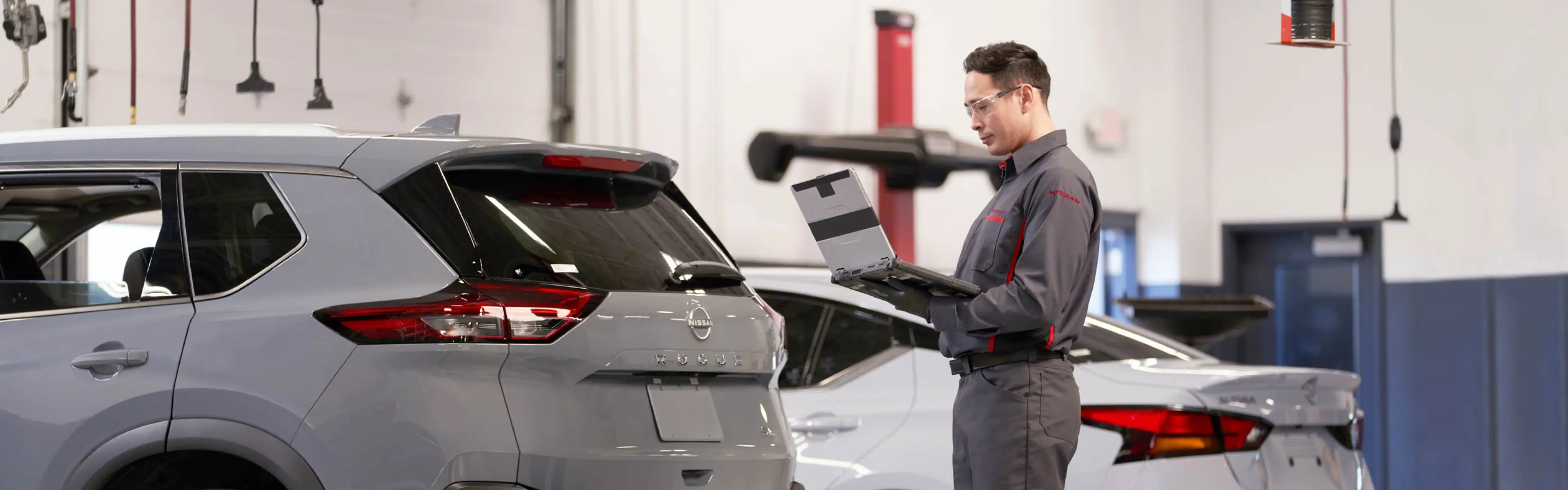 Nissan trained technician standing with service laptop viewing vehicle information while in service garage