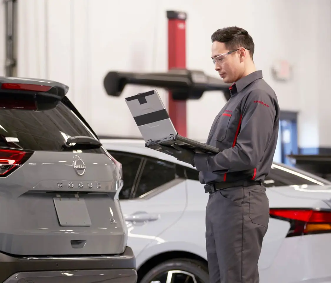 Nissan trained technician standing with service laptop viewing vehicle information while in service garage