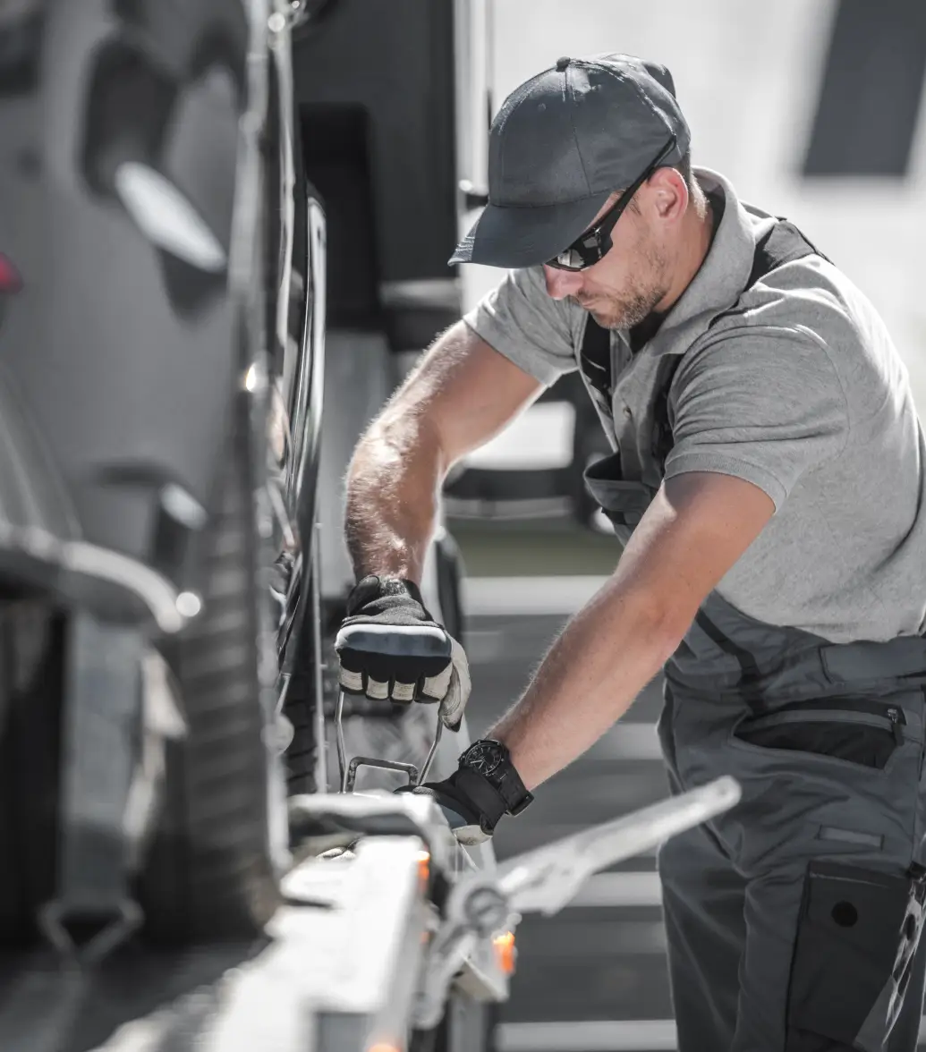 Man in a cap and gloves securing a car onto a tow truck.