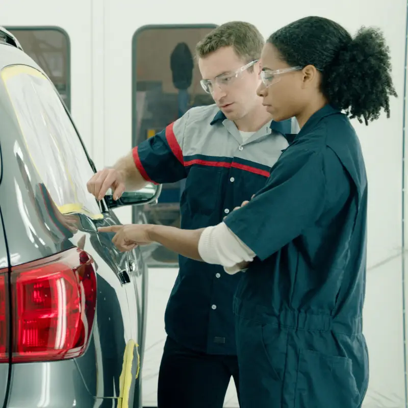 Two technicians wearing safety glasses inspecting the rear of a vehicle.