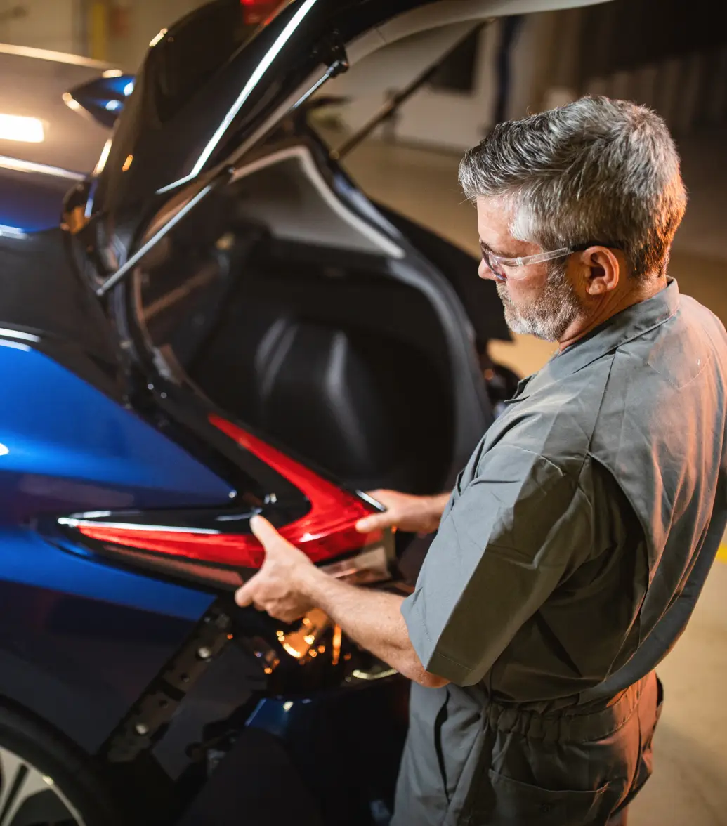 Mechanic adjusting the taillight of a blue car in a garage.